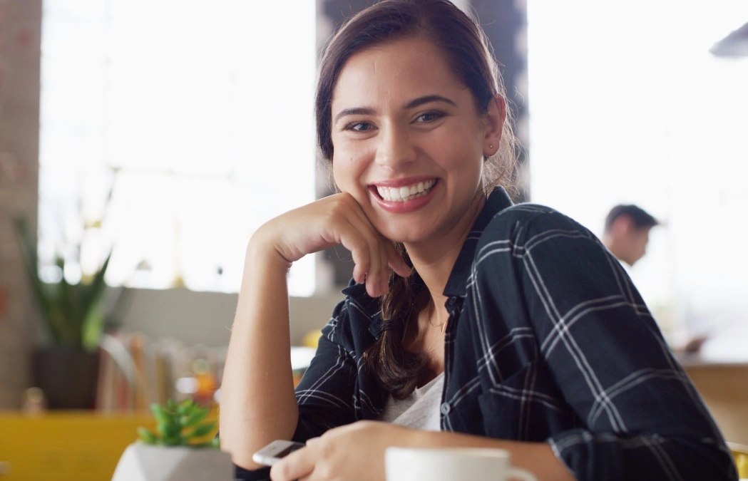 Portrait, smile and woman in coffee shop for relax, peace and calm on weekend break with phone. Face, cafeteria and confident customer in restaurant for service, hospitality and travel on holiday