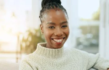 Happy, smile and portrait of black woman on a sofa for relaxing and positive attitude in living room. Excited, calm and young African female person sitting and resting in the lounge of apartment.