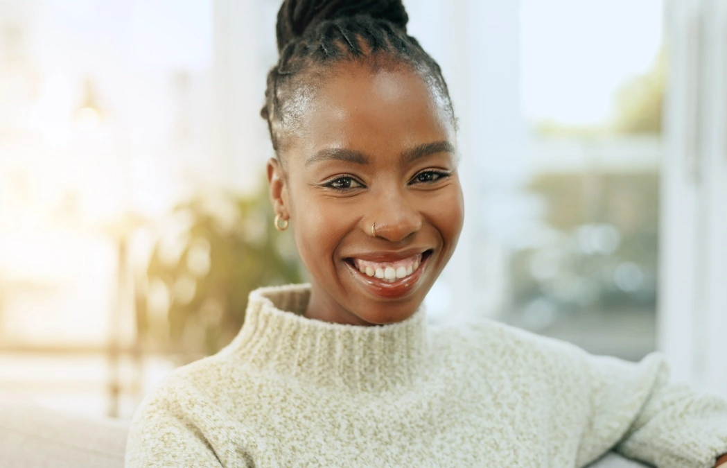 Happy, smile and portrait of black woman on a sofa for relaxing and positive attitude in living room. Excited, calm and young African female person sitting and resting in the lounge of apartment.